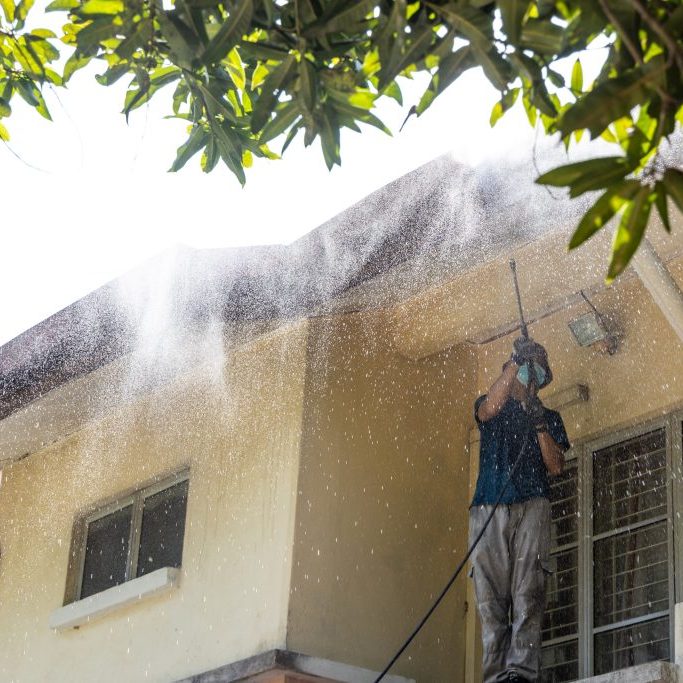 Worker using high pressure water jet spray gun to wash and clean dirt from roof ceiling at residential building